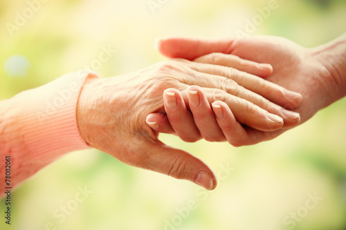 Fotografie, Obraz Old and young holding hands on light background, closeup