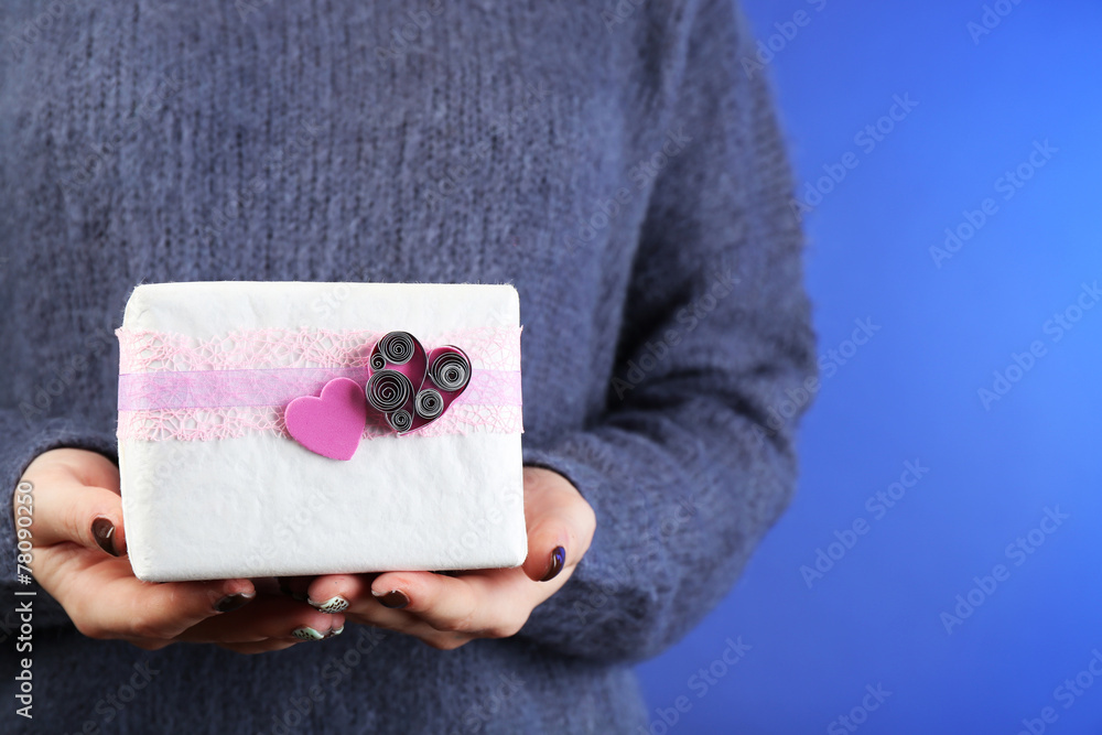 Gift box in female hand on color background