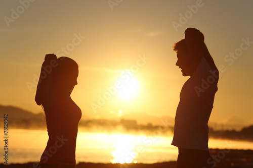 Fotografia Silhouette of a fitness couple stretching at sunrise