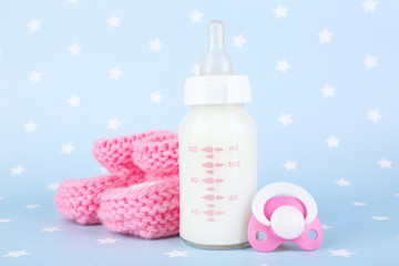 Fototapete - Baby milk bottle, pacifier and babys bootees on blue background