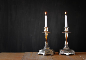 two candlesticks with burning candels over wooden table and blac