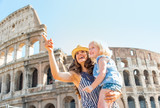 Fototapeta  - Happy mother and baby girl sightseeing near colosseum in rome
