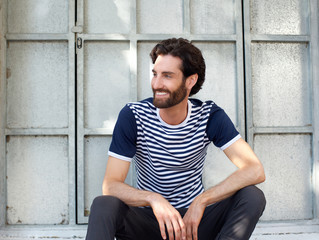 Happy young man sitting on outside frame of a window