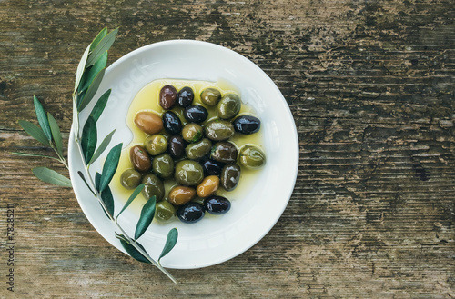 Cuadros en Lienzo Un plato de aceitunas mediterráneas en aceite de oliva con una rama de ol