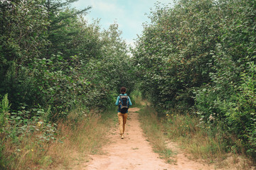 Wall Mural - Hiker woman walking on path among trees in summer