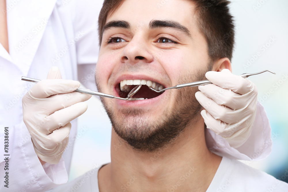 Examine of young man by dentist on light blurred background