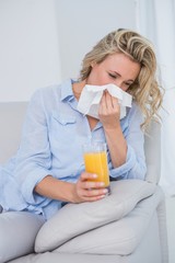 Wall Mural - Blonde sneezing on tissue and holding glass of orange juice