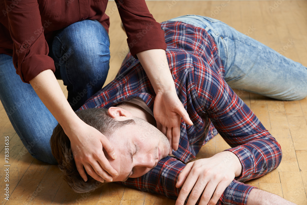 Woman Placing Man In Recovery Position After Accident - obrazy, fototapety, plakaty 