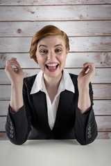 Poster - Composite image of excited redhead businesswoman sitting at desk