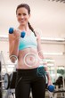 © WavebreakmediaMicro - Composite image of fit smiling brunette lifting blue dumbbells