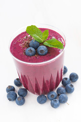 Wall Mural - blueberry milkshake in a glass on white table, close-up