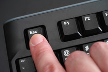 Finger pushing Esc key on black keyboard