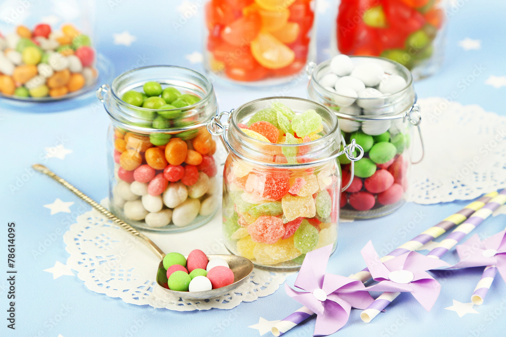 Multicolor candies in glass jars on colorful background