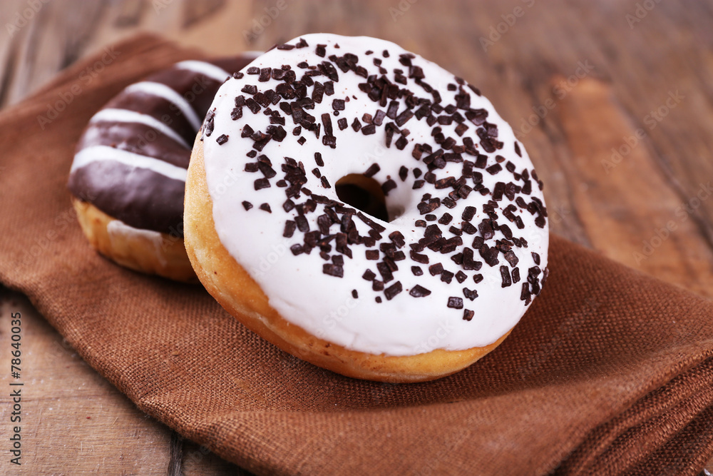 Delicious donuts with icing on napkin on wooden background