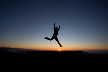 silhouetted man jumping on mountain in sunset