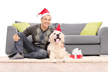 Poster - Man and a dog with Santa hats sitting by a sofa