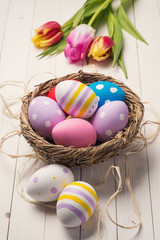 Wall Mural - Fresh tulips and colorful easter eggs in a nest on a wooden tabl