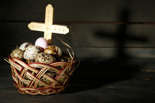 Bird Eggs In Wicker Basket With Wooden Cross On Dark Background