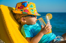 Boy Kid In Armchair With Juice Glass On Beach