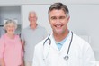 © WavebreakmediaMicro - Doctor smiling with senior couple in background at clinic
