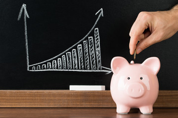 Close-up Of A Hand Putting A Coin Into Piggy Bank