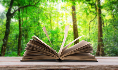 Open book  on wood table in green forest