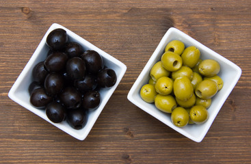 Bowls with green and black olives on wooden table top views