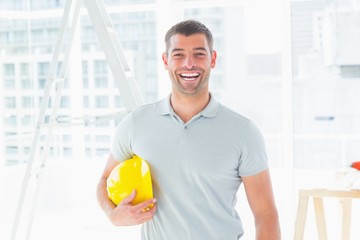 Poster - Cheerful handyman holding hardhat at construction site