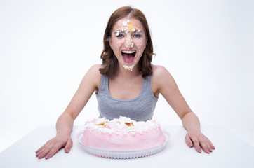 Poster - Cheerful young woman sitting at the table with cake at her face