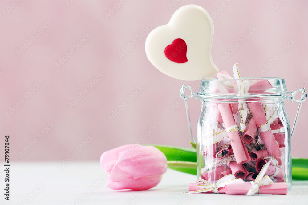 Jar of papers with sweet heart on table on bright background