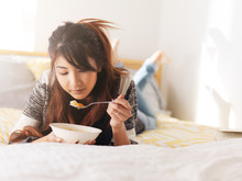 Asian Teenager Eating Chicken Soup In Bed