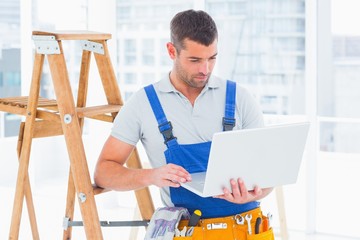 Poster - Repairman using laptop by ladder in office