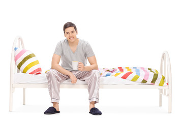 Canvas Print - Guy drinking his morning coffee seated on a bed