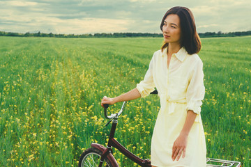 Wall Mural - Beautiful woman resting with a bicycle on summer meadow