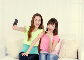 Wall Mural - Two girls sitting on sofa and making photo on mobile phone