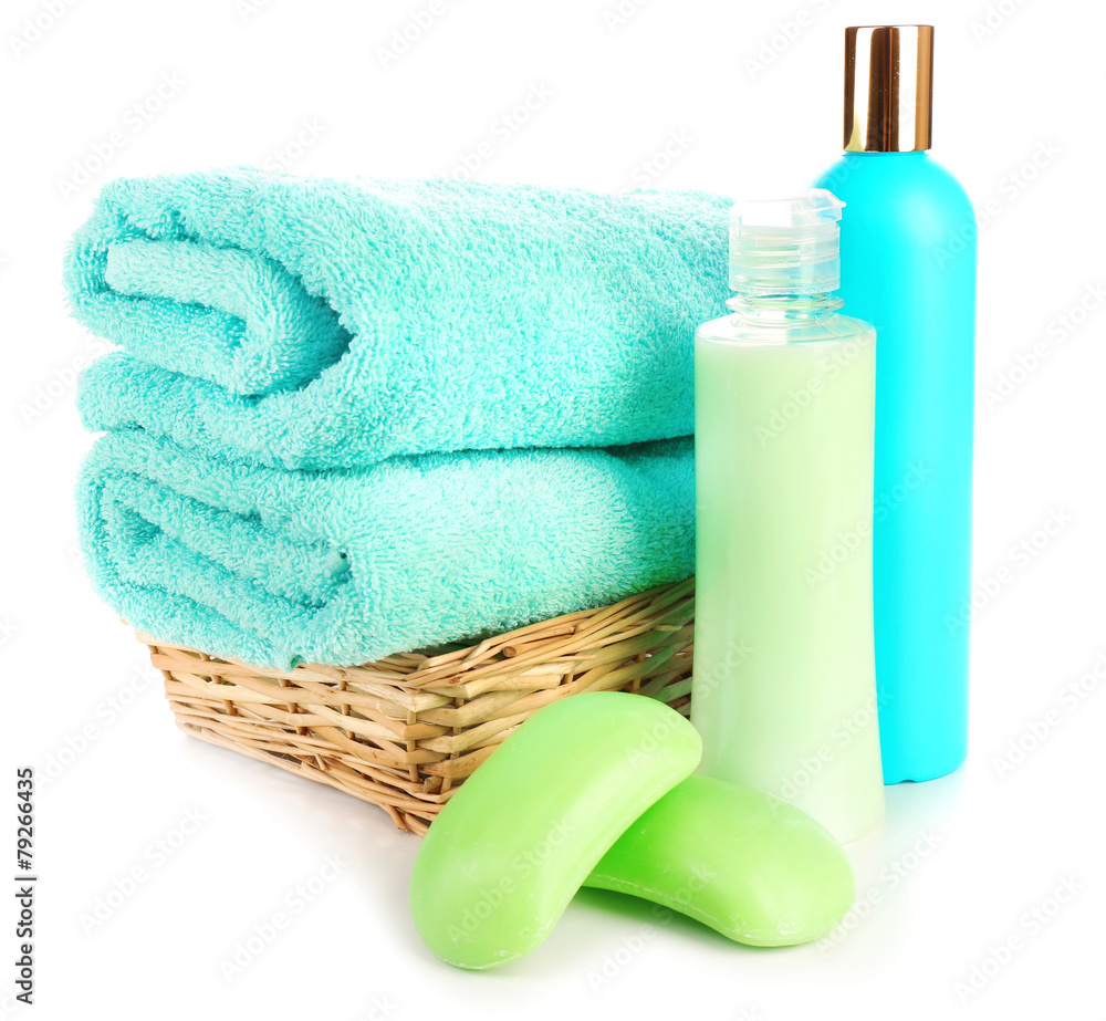 Towels in wicker basket with shampoo bottles and soap isolated