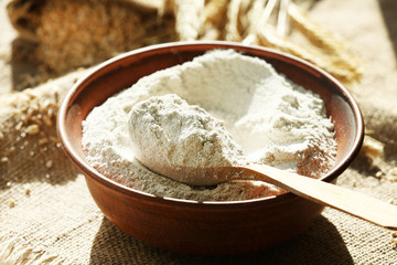 Wall Mural - Bowl of flour with wooden spoon on burlap cloth background