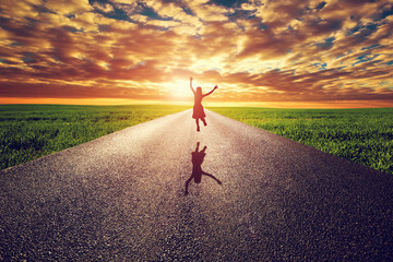 Happy woman jumping on long straight road, way towards sun