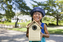 Young Girl Wearing A Summer Dress And Sun Hat, Holding A Bird House.