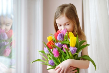 Wall Mural - Adorable little girl holding tulips by the window