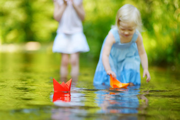 Two sisters playing with paper boats by a river