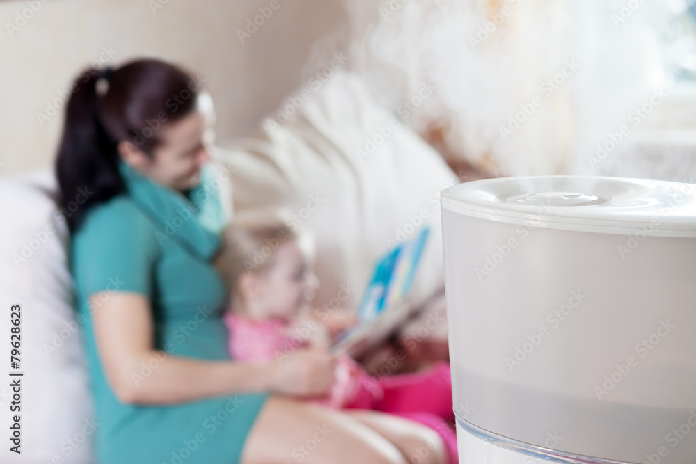 Mother reading book to her daughter on the background of humidif