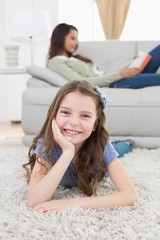 Wall Mural - Happy girl lying on rug while mother relaxing at home