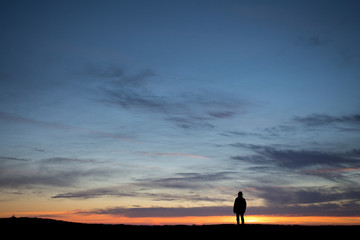 Wall Mural - silhouetted elderly man standing in front of a sunset sky