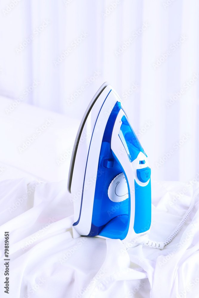 Electric iron and shirt on ironing board in room