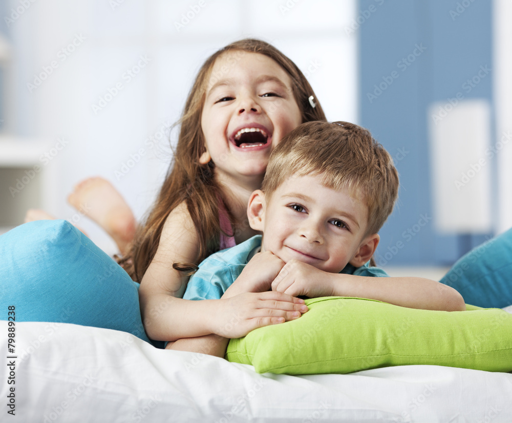Portrait of two smiling siblings lying on cushions - obrazy, fototapety, plakaty 