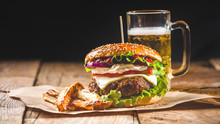Fresh And Juicy Hamburger On A Paper Pad With A Beer On A Wooden