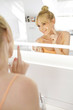 © Westend61 - Smiling woman looking at her mirror image while applying face cream