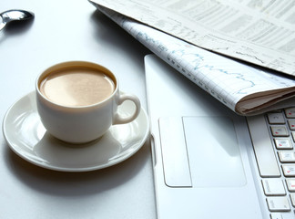 Cup of coffee near the laptop and newspapers