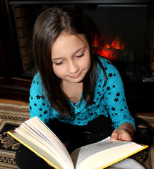 Little cute girl reading book by the fireplace